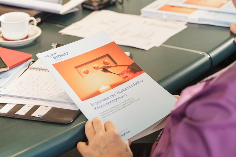 Unterlagen und Terminkalender auf einem Tisch - Hände halten eine Broschüre zum Thema Krisenmanagement