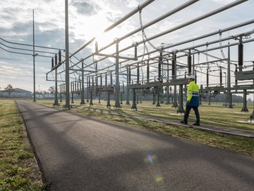 Mitarbeiter mit Helm und Warnschutzjacke bei Anlagen im Umspannwerk unter freiem Himmel Mitarbeiter mit Helm und Warnschutzjacke bei Anlagen im Umspannwerk unter freiem Himmel