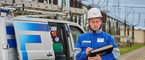 Mitarbeiter in blauer Arbeitskleidung mit Unterlagen vor einem Fahrzeug im Umspannwerk Mitarbeiter in blauer Arbeitskleidung mit Unterlagen vor einem Fahrzeug im Umspannwerk