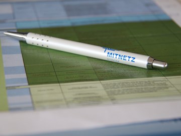 Kugelschreiber mit MITNETZ STROM-Logo auf Unterlagen - Nahaufnahme Kugelschreiber mit MITNETZ STROM-Logo auf Unterlagen - Nahaufnahme