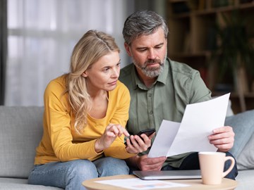 Verheiratetes Paar mittleren Alters plant gemeinsam Budget, liest Papiere und berechnet Ausgaben Verheiratetes Paar mittleren Alters plant gemeinsam Budget, liest Papiere und berechnet Ausgaben