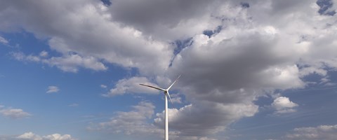 Windrad auf einem grünen Feld vor einem Wald mit wolkigem Himmel Windrad auf einem grünen Feld vor einem Wald mit wolkigem Himmel