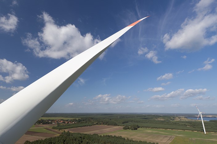 Flügel eines Windrads vor einer Landschaft mit viel blauem Himmel und einigen Wolken Flügel eines Windrads vor einer Landschaft mit viel blauem Himmel und einigen Wolken