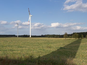 Zwei Windräder auf einem Feld, auf das der Schatten eines weiteren Windrades fällt Zwei Windräder auf einem Feld, auf das der Schatten eines weiteren Windrades fällt