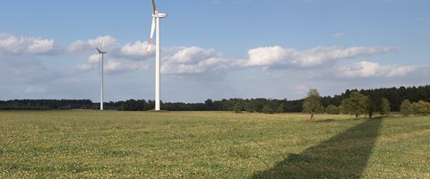 Zwei Windräder auf einem Feld, auf das der Schatten eines weiteren Windrades fällt Zwei Windräder auf einem Feld, auf das der Schatten eines weiteren Windrades fällt
