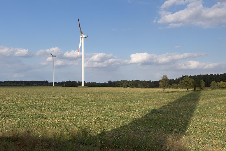 Zwei Windräder auf einem Feld, auf das der Schatten eines weiteren Windrades fällt Zwei Windräder auf einem Feld, auf das der Schatten eines weiteren Windrades fällt