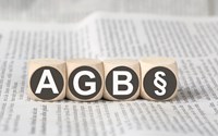 Vier Holzwürfel auf einer Zeitung zeigen die Abkürzung AGB und das Paragrafenzeichen Vier Holzwürfel auf einer Zeitung zeigen die Abkürzung AGB und das Paragrafenzeichen
