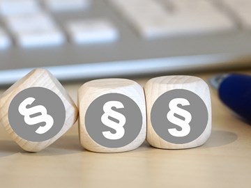 Vier Holzwürfel auf einem Schreibtisch neben einem Kugelschreiber vor einer Tastatur zeigen alle das Paragrafenzeichen Vier Holzwürfel auf einem Schreibtisch neben einem Kugelschreiber vor einer Tastatur zeigen alle das Paragrafenzeichen